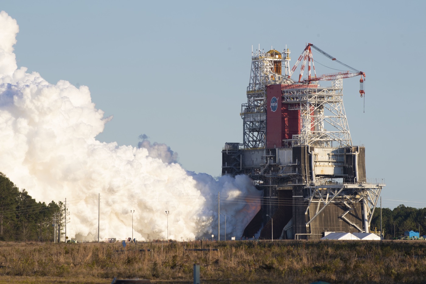 Four RS-25 rocket engines firing at the base of the SLS core stage on a test stand, producing a huge white steam cloud